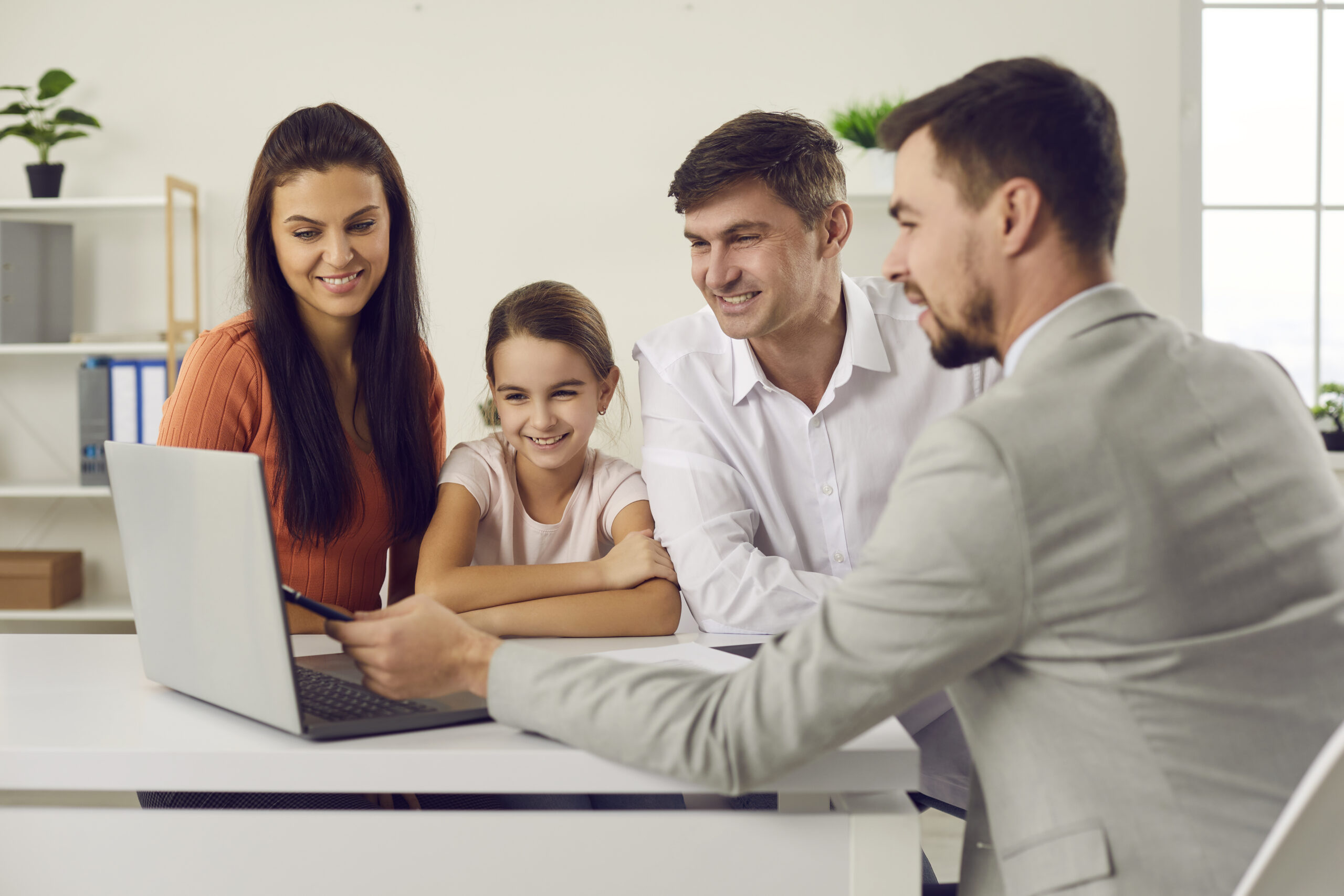 Two office men pointing to a laptop screen for a young girl and an office girl