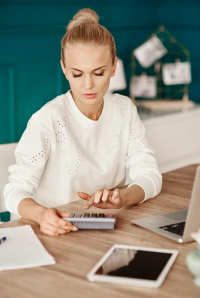 Financial advisor works on tax computation using calculator and digital tools at wooden desk