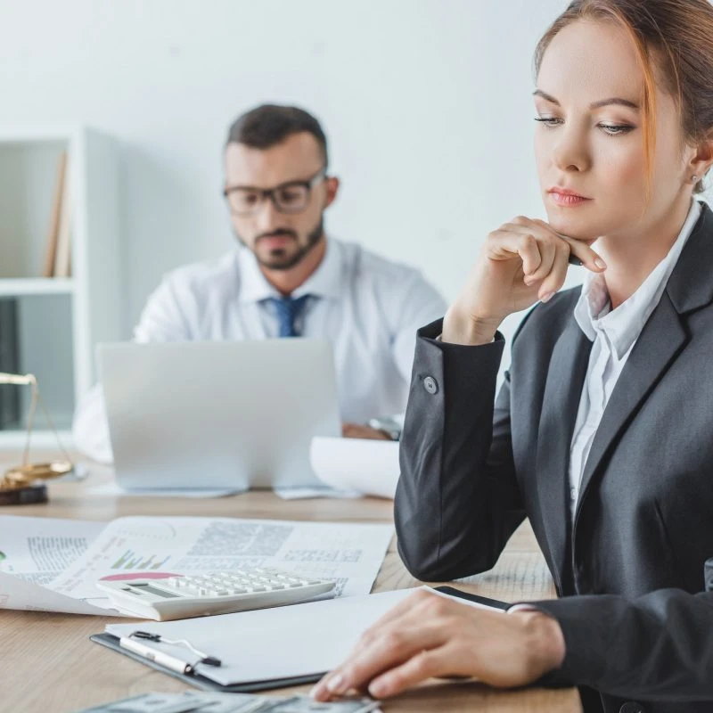 Female expert accountant for lottery winners thinking while male colleague works on laptop behind
