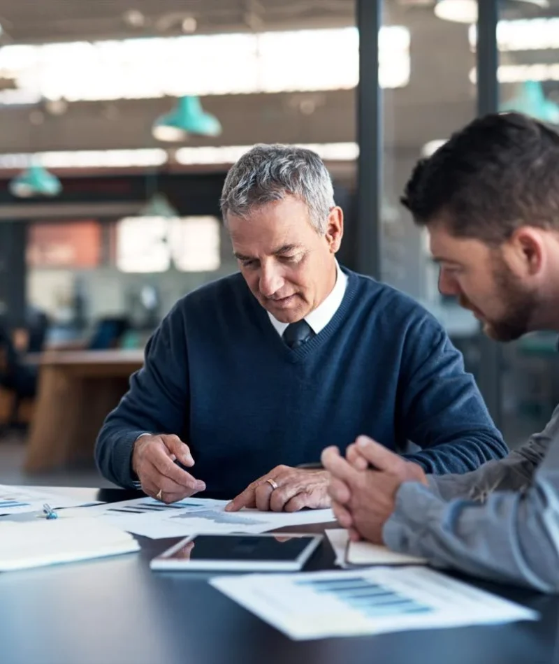 A senior accountant and a junior accountant for actors in the office reviewing data from a paper