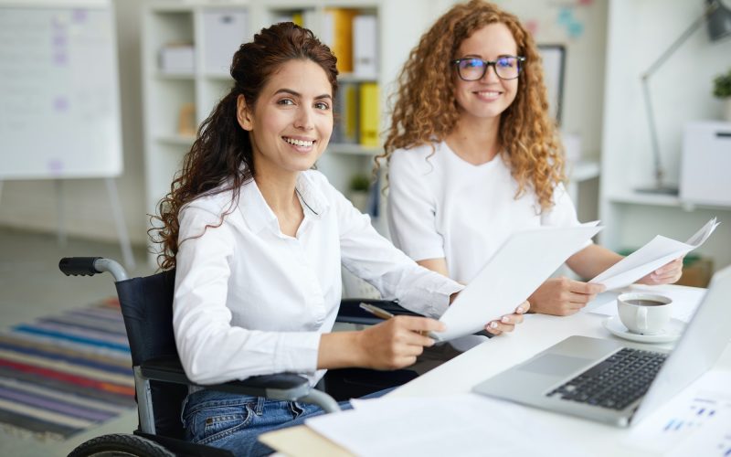 Two office girls in white dresses smiling with a laptop on the table
