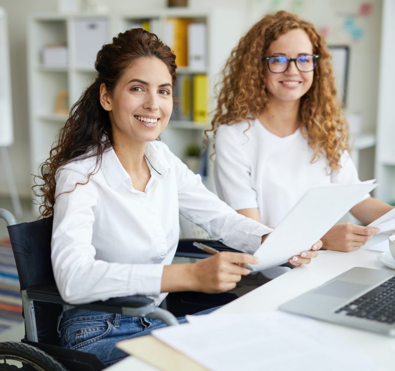 Two office girls in white dresses smiling with a laptop on the table