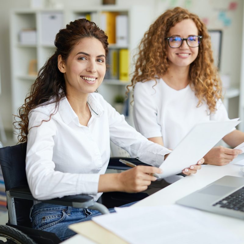 Two office girls in white dresses smiling with a laptop on the table
