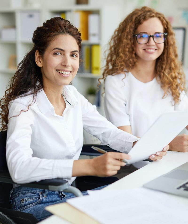 Two office girls in white dresses smiling with a laptop on the table