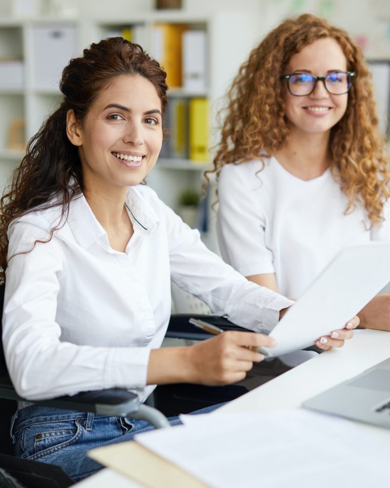 Two office girls in white dresses smiling with a laptop on the table