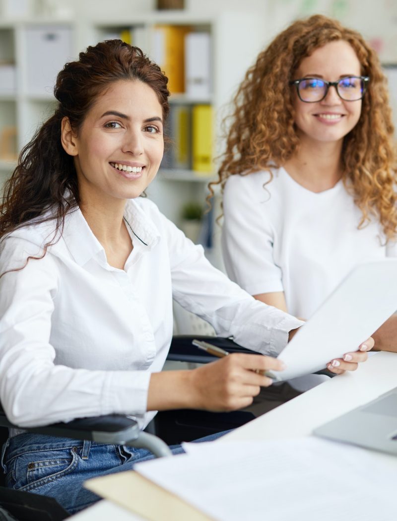 Two office girls in white dresses smiling with a laptop on the table