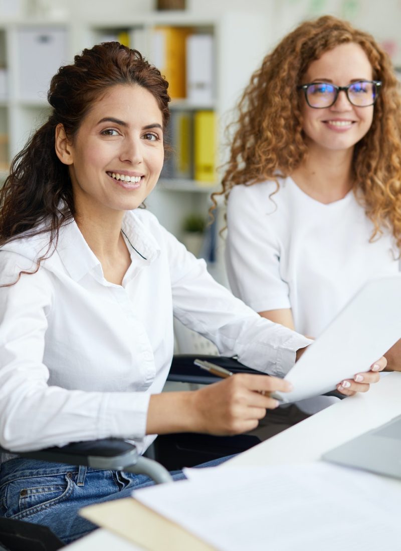 Two office girls in white dresses smiling with a laptop on the table