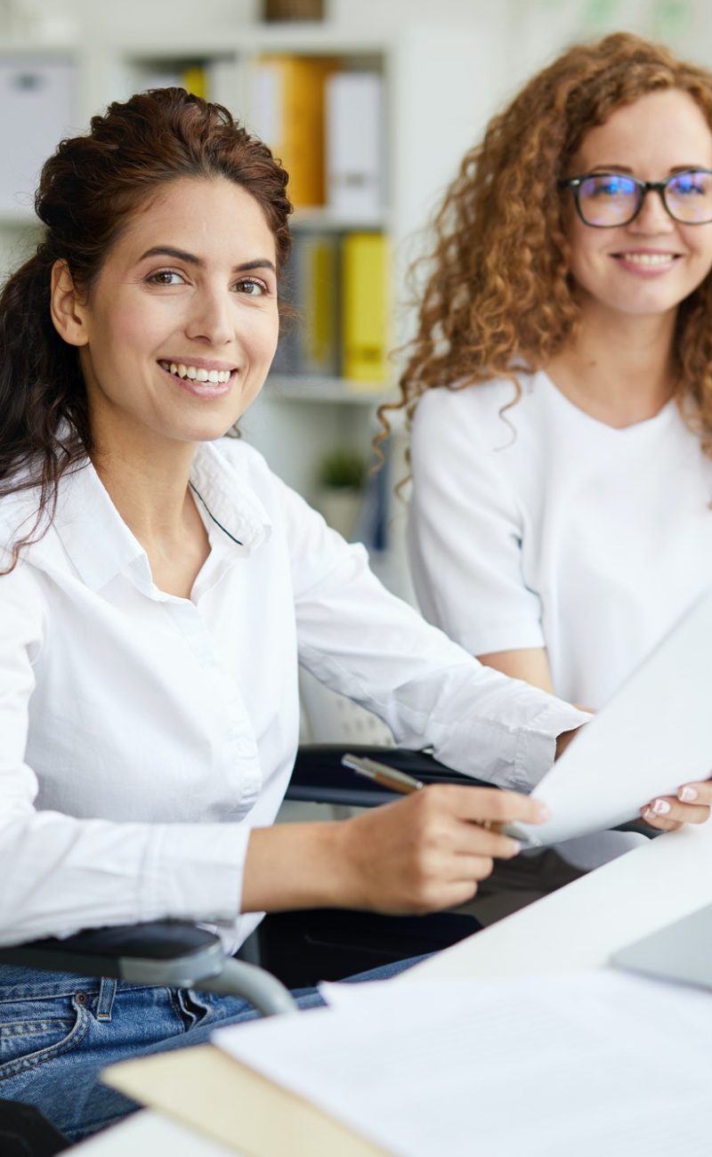 Two office girls in white dresses smiling with a laptop on the table