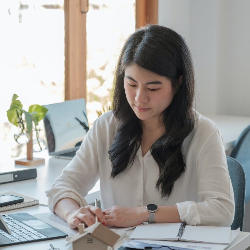 Business asian woman using calculating interest, taxes and profits to invest in real estate and home Office girl wearing a white shirt doing her job of bookkeeping and accounting