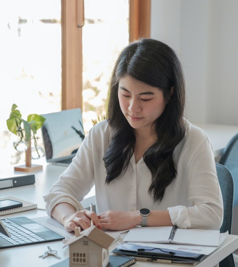 Business asian woman using calculating interest, taxes and profits to invest in real estate and home Office girl wearing a white shirt doing her job of bookkeeping and accounting