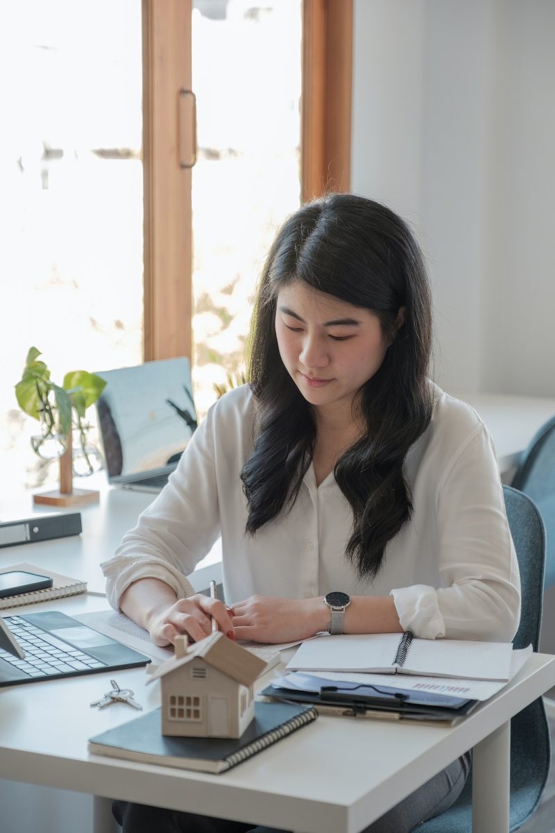 Business asian woman using calculating interest, taxes and profits to invest in real estate and home Office girl wearing a white shirt doing her job of bookkeeping and accounting
