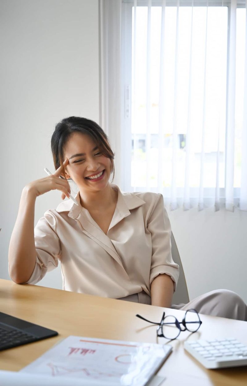Portrait of happy female accountant sitting at her workplace and laughing.