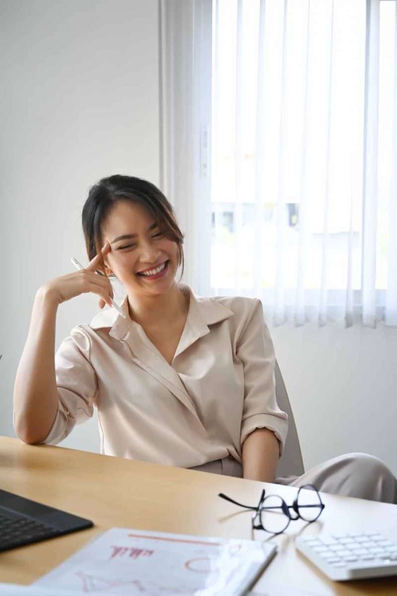 Portrait of happy female accountant sitting at her workplace and laughing.