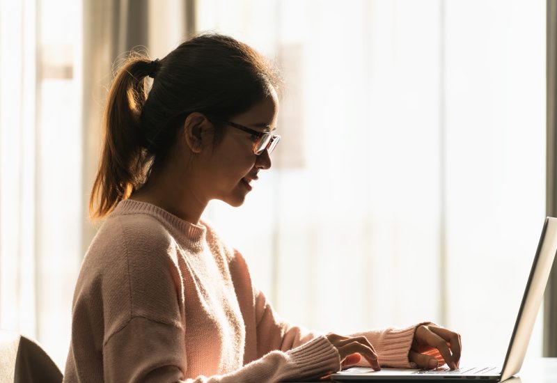 Side view happy asian accounting student with eyewear looking/smiling at computer