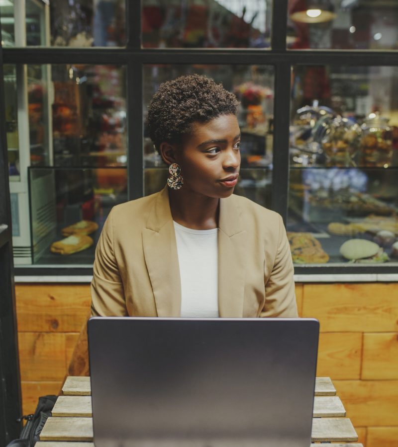Smiling Black woman sitting at table with laptop in cafe Bookkeeper for a dentist, a girl with a laptop, looking to the side