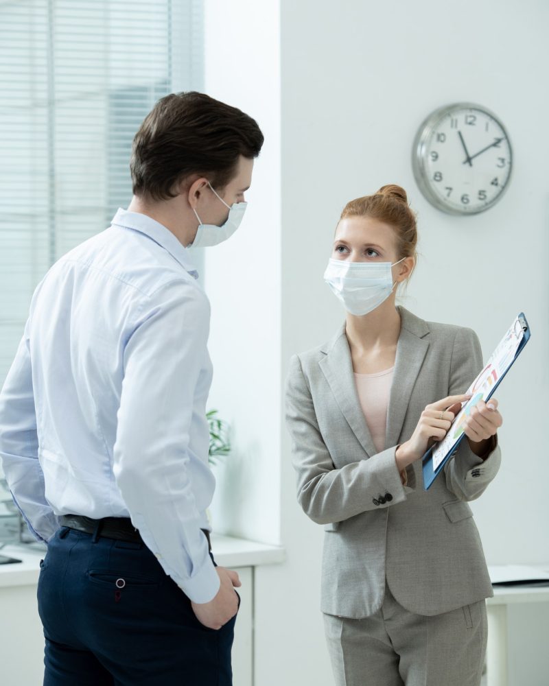 Two young elegant accountants in protective masks discussing financial document, Sole Trader Accountant
