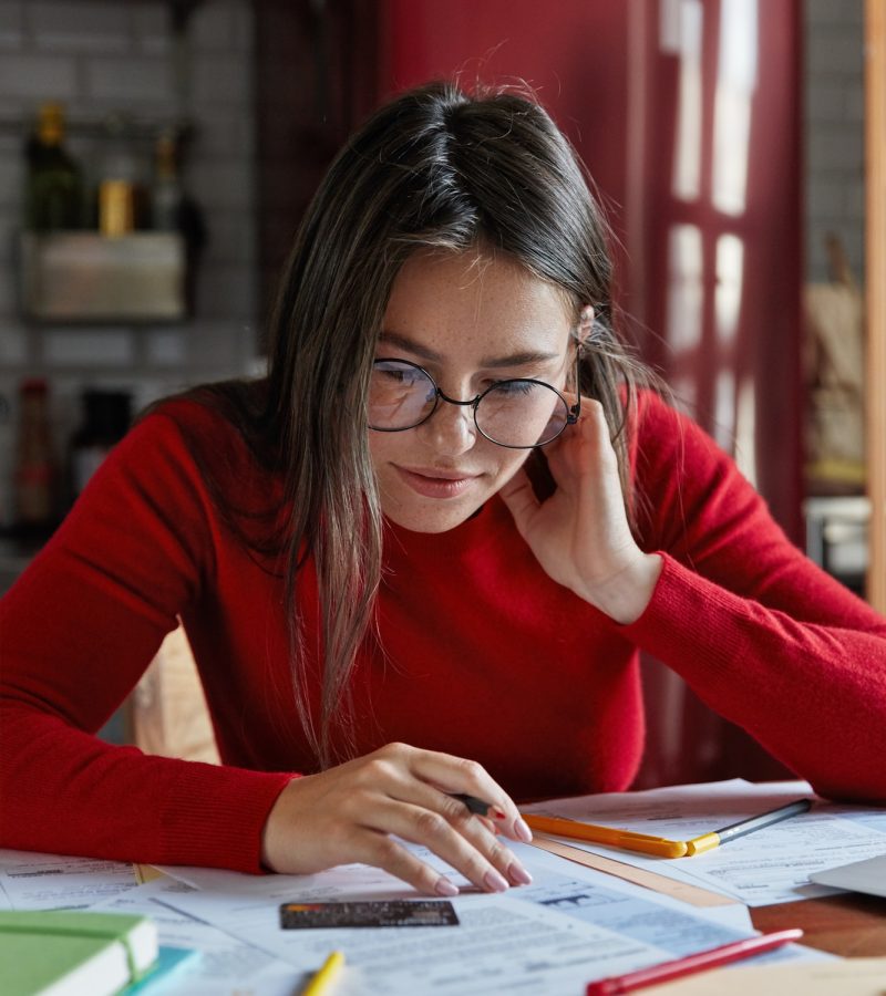 Vertical shot of freckled brunette young housewife sits at home with credit card, accounts costs, accountants for authors
