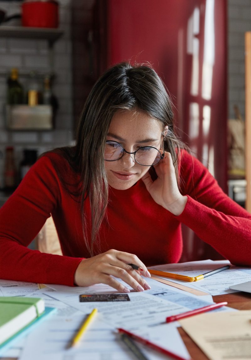 Vertical shot of freckled brunette young housewife sits at home with credit card, accounts costs, ch Vertical shot of freckled brunette young housewife sits at home with credit card, accounts costs, accountants for authors