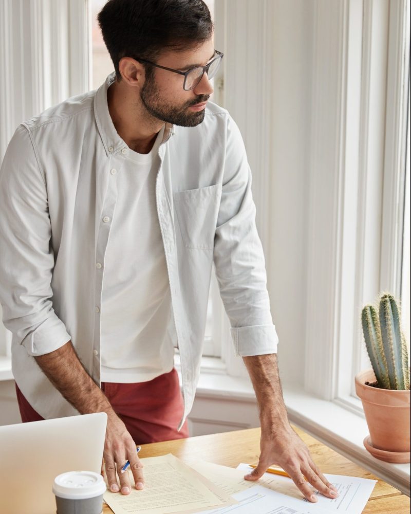 Vertical shot of male coworker cant make right accountings in papers, looks at documents planner, st
