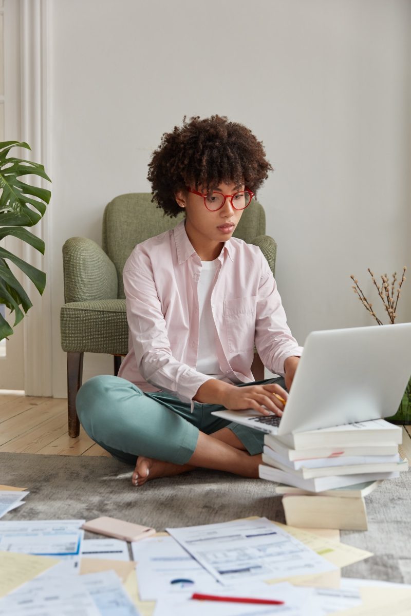 Vertical shot of professional web designer prepares new sketch on laptop computer, wears casual clot