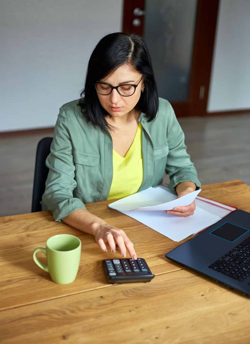Woman accountant sit calculate expenses on calculator at wooden table, modern workplace