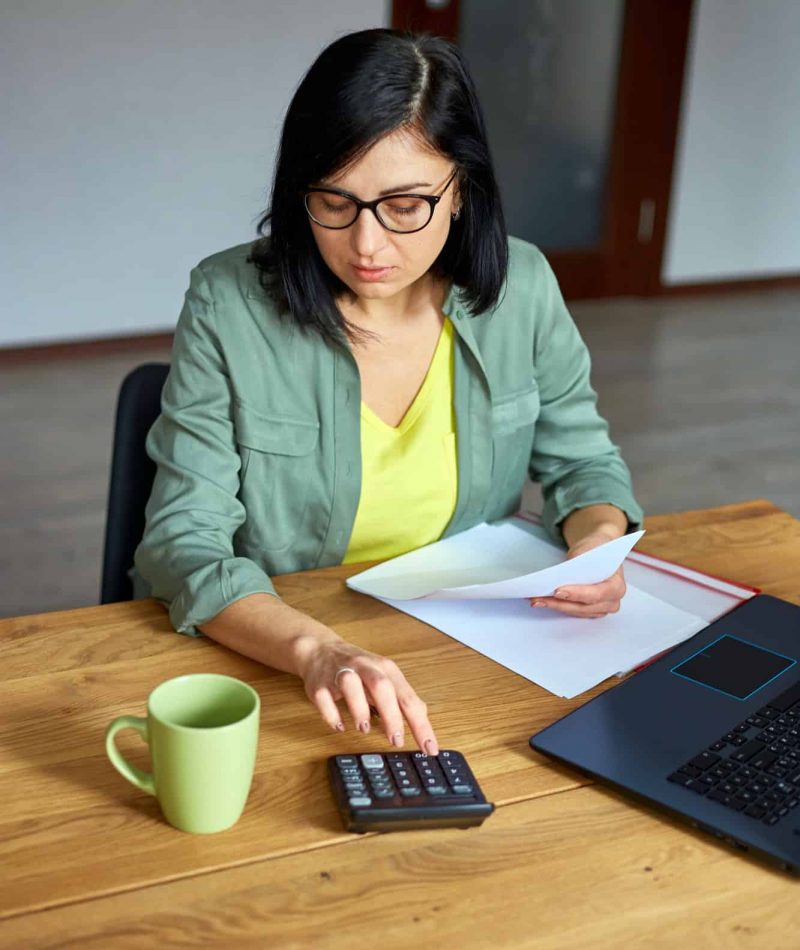 Woman accountant sit calculate expenses on calculator at wooden table, modern workplace