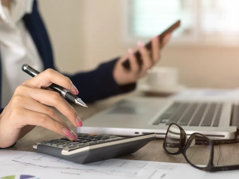 Girl using phone while calculating data on a calculator