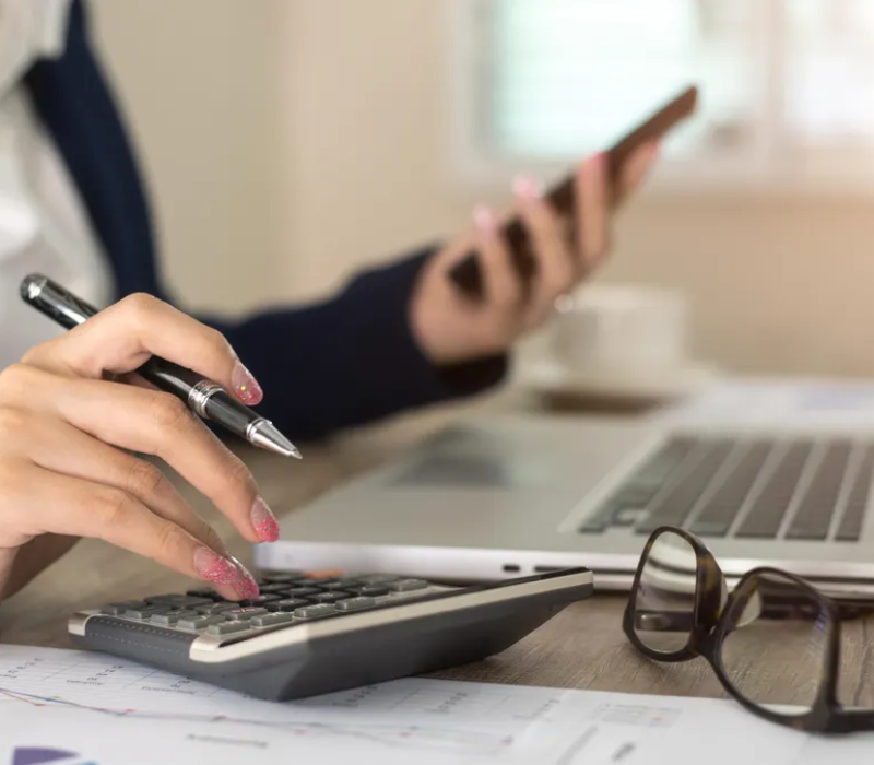 Girl using phone while calculating data on a calculator