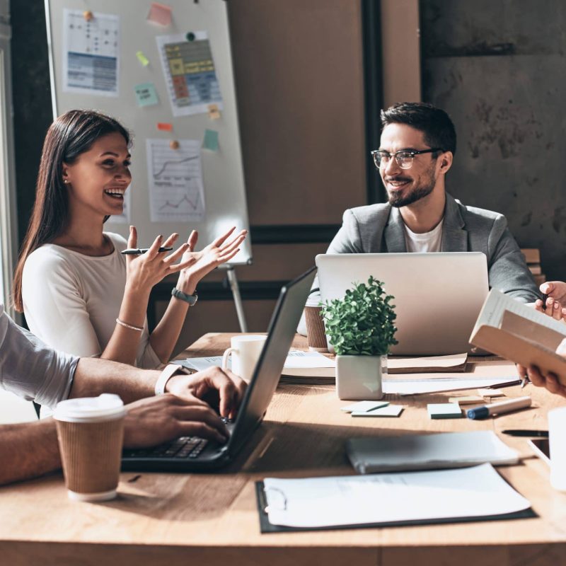 Working together. Group of young modern people in smart casual wear discussing business and smiling while sitting in the creative office Working together. Group of young modern people in smart casual wear discussing business and smiling while sitting in the creative office