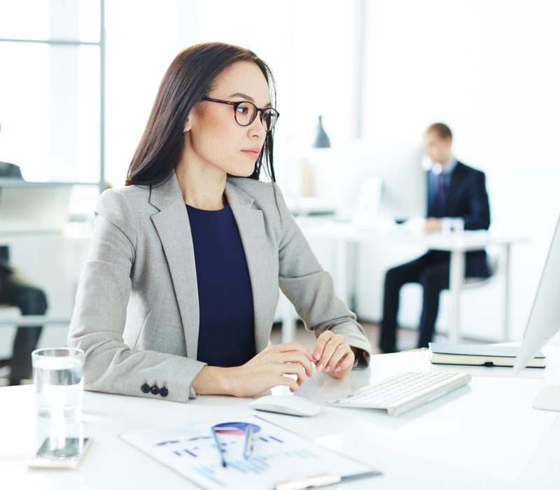 Young accountant A beautiful working girl with glasses, wearing a coat, in the office