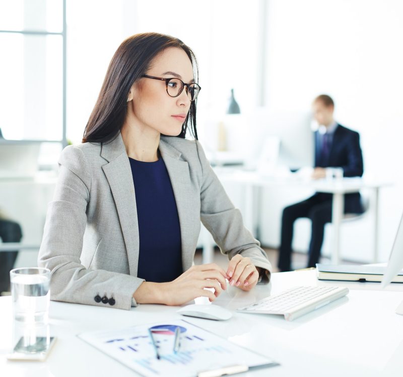 A beautiful working girl with glasses, wearing a coat, in the office