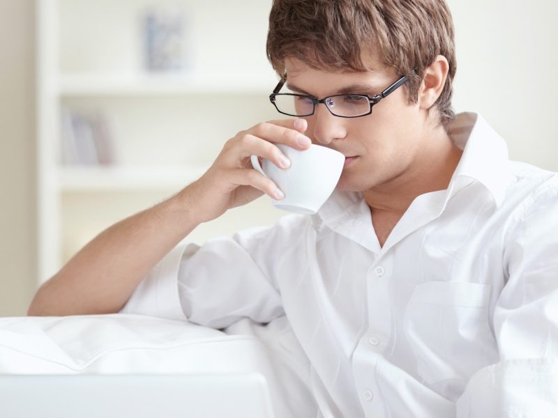 Young man with laptop at home Young accountant and bookkeeper drinking tea and using a laptop