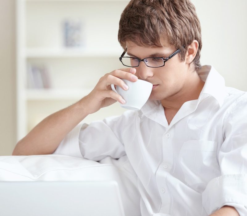 Young accountant and bookkeeper drinking tea and using a laptop