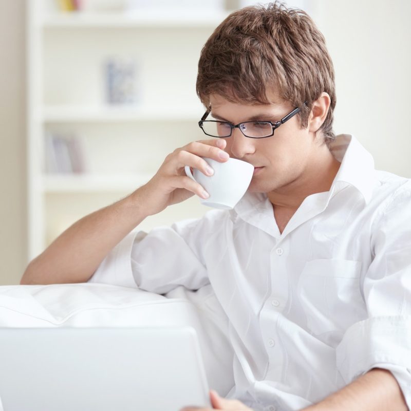 Young accountant and bookkeeper drinking tea and using a laptop