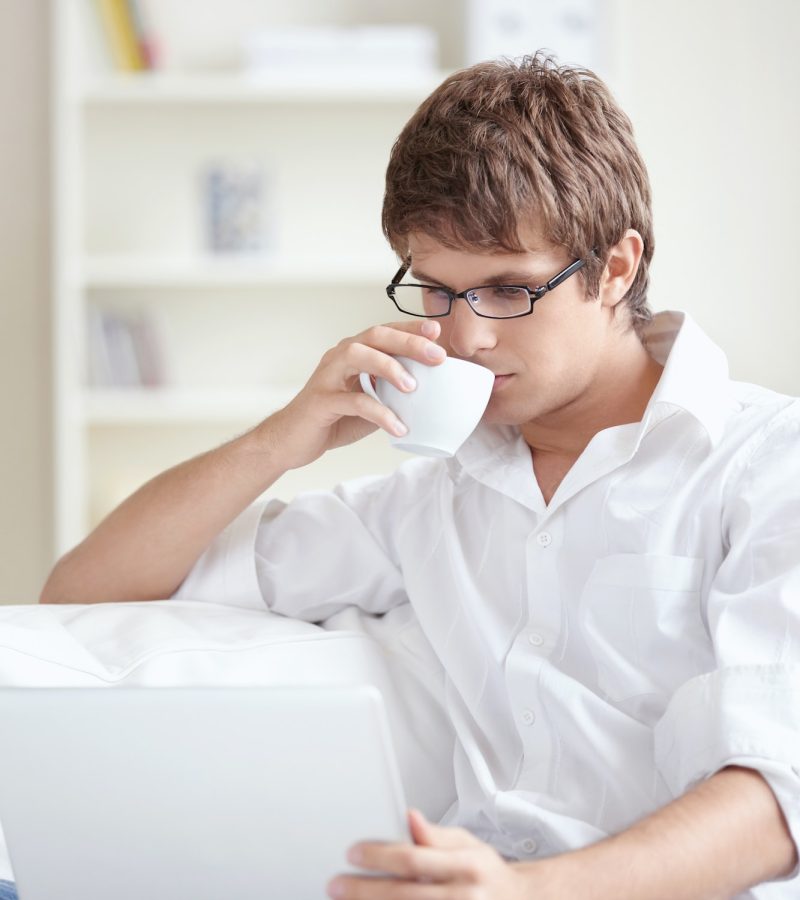 Young accountant and bookkeeper drinking tea and using a laptop