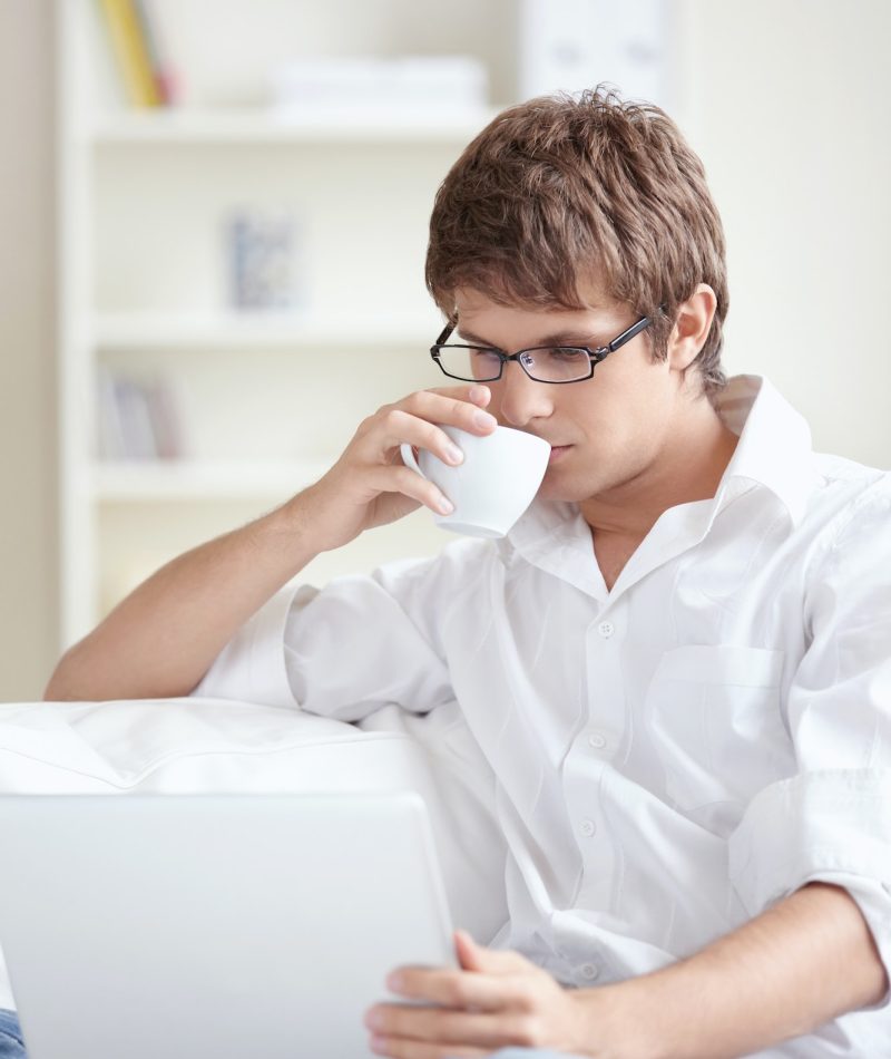 Young accountant and bookkeeper drinking tea and using a laptop