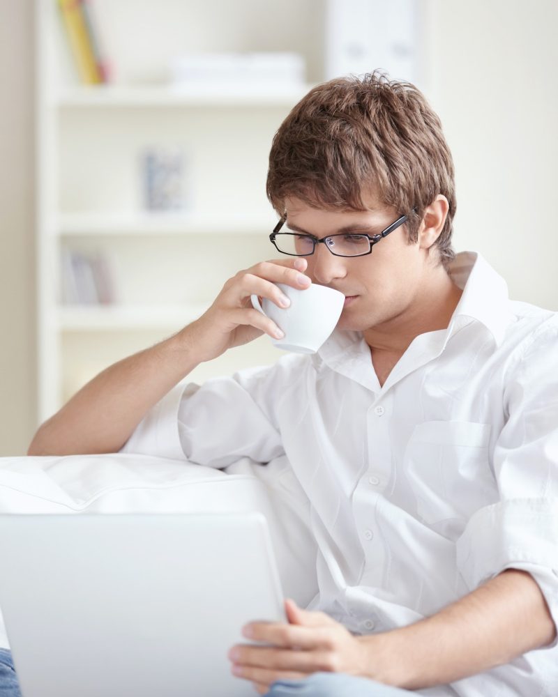 Young man with laptop at home Young accountant and bookkeeper drinking tea and using a laptop