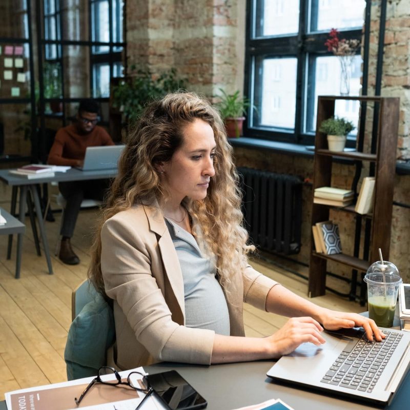 Young serious pregnant accountant sitting by desk in front of laptop Young serious pregnant accountant sitting by desk in front of laptop